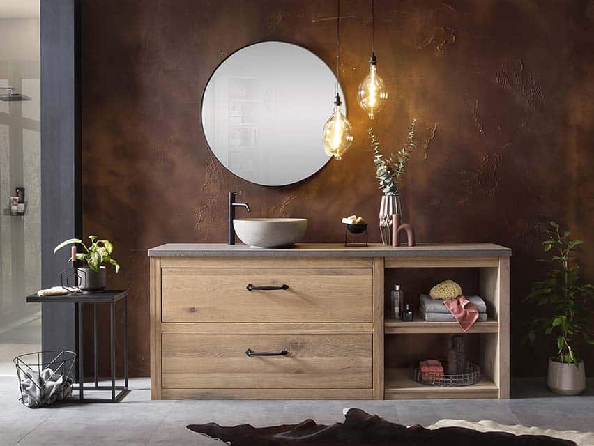 Ein Bild von einem Badmöbel Holz aus massiver Eiche, darauf eine Beton-Waschtischplatte und ein Betonwaschbecken. Über dem Waschbecken hängt eine schwarze Waschbeckenarmatur und an der Wand ist ein schwarzer Spiegel befestigt.