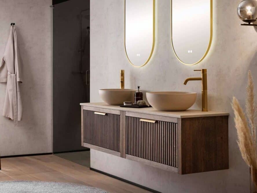Eiken badkamermeubel in 160 cm in de kleur donker eiken. Het meubel is van massief eiken met daarboven een beton beige blad met twee beige betonnen kommen en twee gouden kranen. Boven het badmeubel hangen twee gouden ovalen spiegels