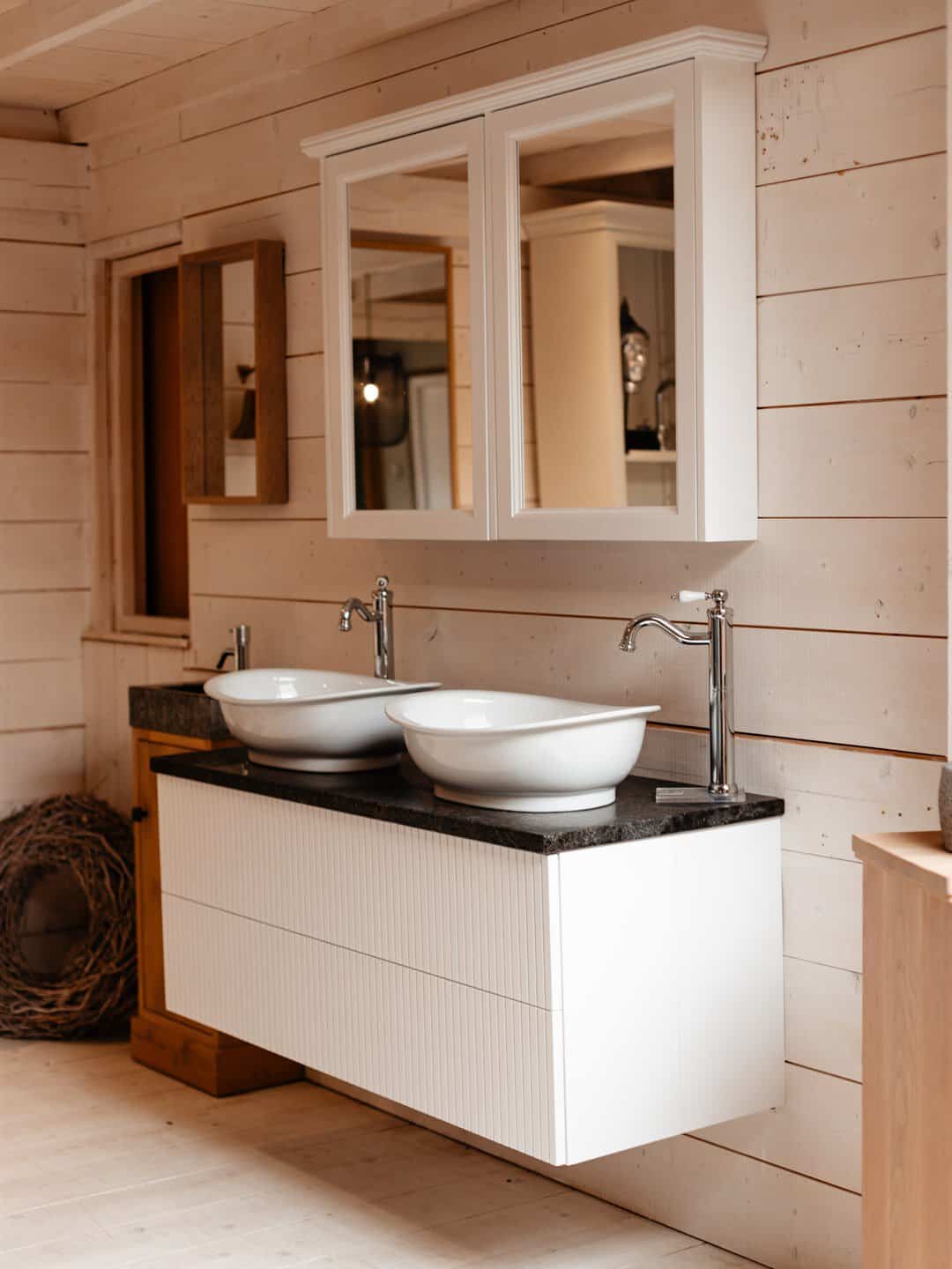 Weißes Möbel mit zwei Aufsatzbecken und Spiegelschrank an einer Holzwand